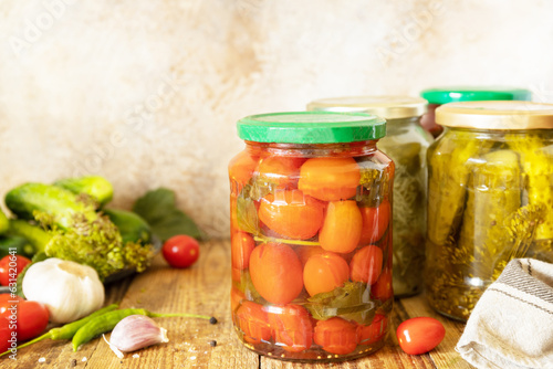 Salted pickled cucumbers and tomatoes preserved canned in glass jar. Home economics, autumn harvest preservation. Healthy homemade fermented food. Copy space.