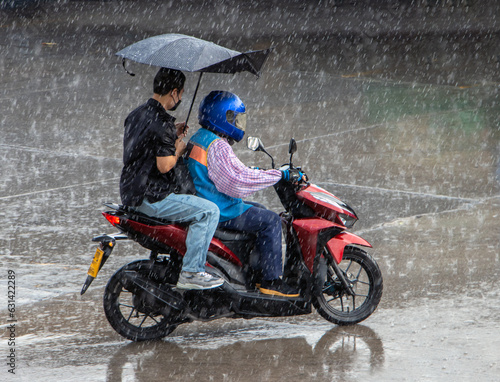 Leinwand Poster A motorcycle taxi driver with passenger rides in a heavy rain, Thailand