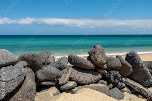Copy on foreground on black lava stones. In the background, the ocean and the white sand of Playa Mal Nombre, in the south of Fuerteventura island. Turquoise sea streaked of blue, clear blue sky.