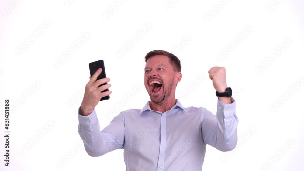 Young bearded man takes out mobile phone from pocket and exclaims happily looking at screen. Guy shouts and waves fists joyfully receiving win notification Young bearded man takes out mobile phone from pocket and exclaims happily looking at screen. Guy shouts and waves fists joyfully receiving win notification