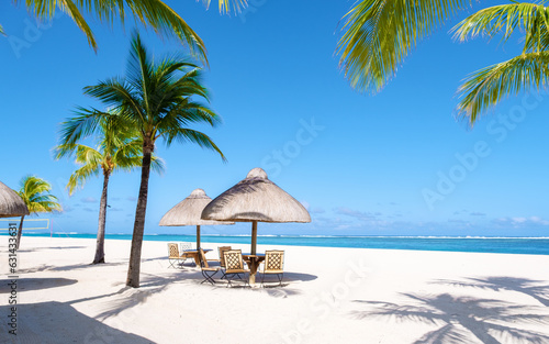 Fototapeta Naklejka Na Ścianę i Meble -  Le Morne beach Mauritius Tropical beach with palm trees and white sand blue ocean and beach beds with umbrellas, sun chairs, and parasols under a palm tree 