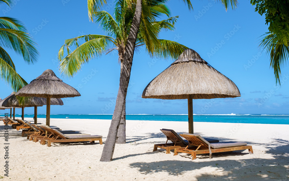 Le Morne beach Mauritius Tropical beach with palm trees and white sand blue ocean and beach beds with umbrellas, sun chairs, and parasols under a palm tree at a tropical beach