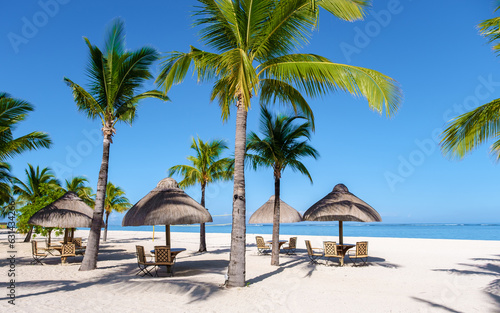 Le Morne beach Mauritius Tropical beach with palm trees and white sand blue ocean and beach beds with umbrellas, sun chairs, and parasols under a palm tree at a tropical beach. Mauritius Le Morne © Chirapriya