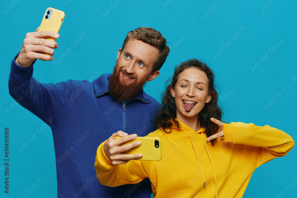 Woman and man funny couple with phones in hand taking selfies crooked smile fun, on blue background. The concept of real family relationships, talking on the phone, work online.