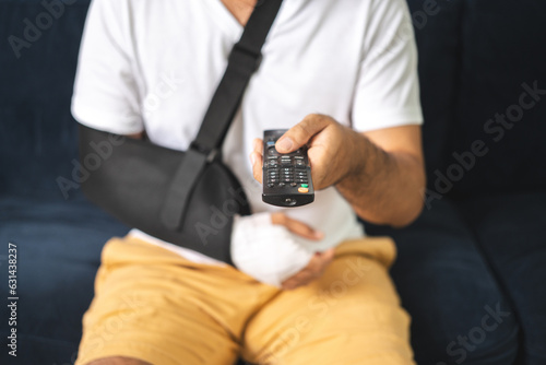 Social security and health insurance concept. Young Man suffer pain from accident fracture broken bone injury with arms splints in cast sling support arm watching tv in living room.