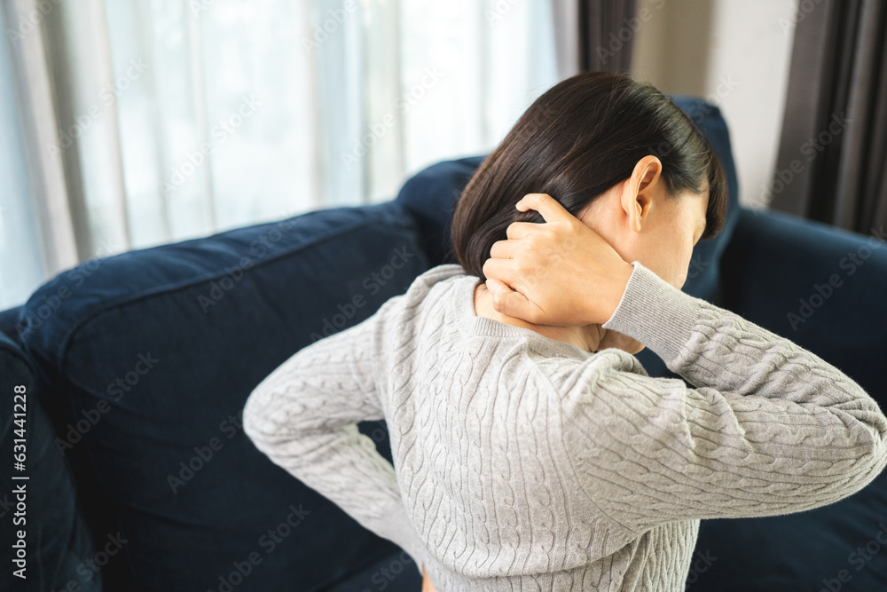 Young woman has problem with structural posture back neck and shoulder pain. Massaged her neck and shoulders for relief. reduce muscle tension on sofa couch in living room Young woman has problem with structural posture back neck and shoulder pain. Massaged her neck and shoulders for relief. reduce muscle tension on sofa couch in living room