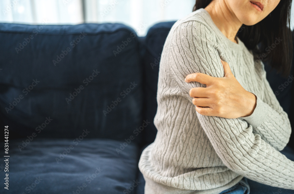 Fototapeta premium Young woman has problem with structural posture arms elbow shoulder pain. Massage her elbow and shoulders for relief. reduce muscle tension on sofa couch in living room