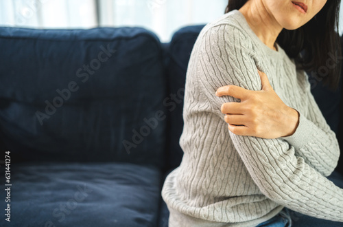 Young woman has problem with structural posture arms elbow shoulder pain. Massage her elbow and shoulders for relief. reduce muscle tension on sofa couch in living room photo