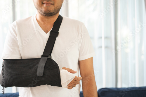 Social security and health insurance concept. Young Man suffer pain from accident fracture broken bone injury with arms splints in cast sling support arm in living room. photo