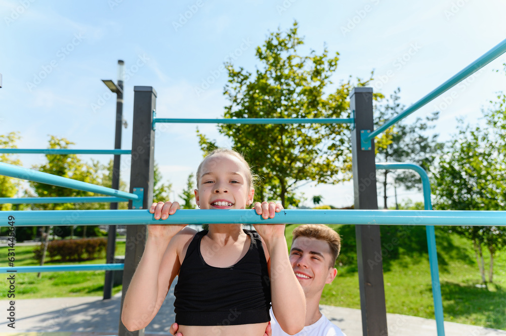 The girl pulls herself up on the horizontal bar with a trainer The girl pulls herself up on the horizontal bar with a trainer