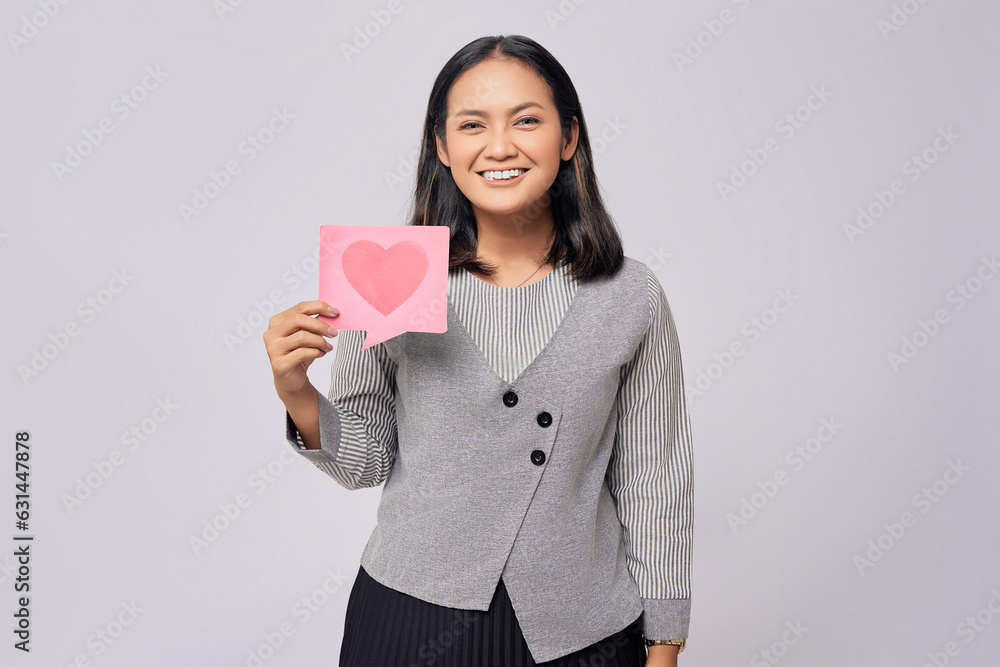 Smiling happy young Asian woman holding a heart form-like icon sign from social network media feedback isolated on grey background Smiling happy young Asian woman holding a heart form-like icon sign from social network media feedback isolated on grey background