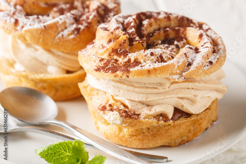 Classic French cake Paris Brest from choux pastry with cream decorated with powdered sugar and cocoa close-up in a plate on the table. Horizontal photo