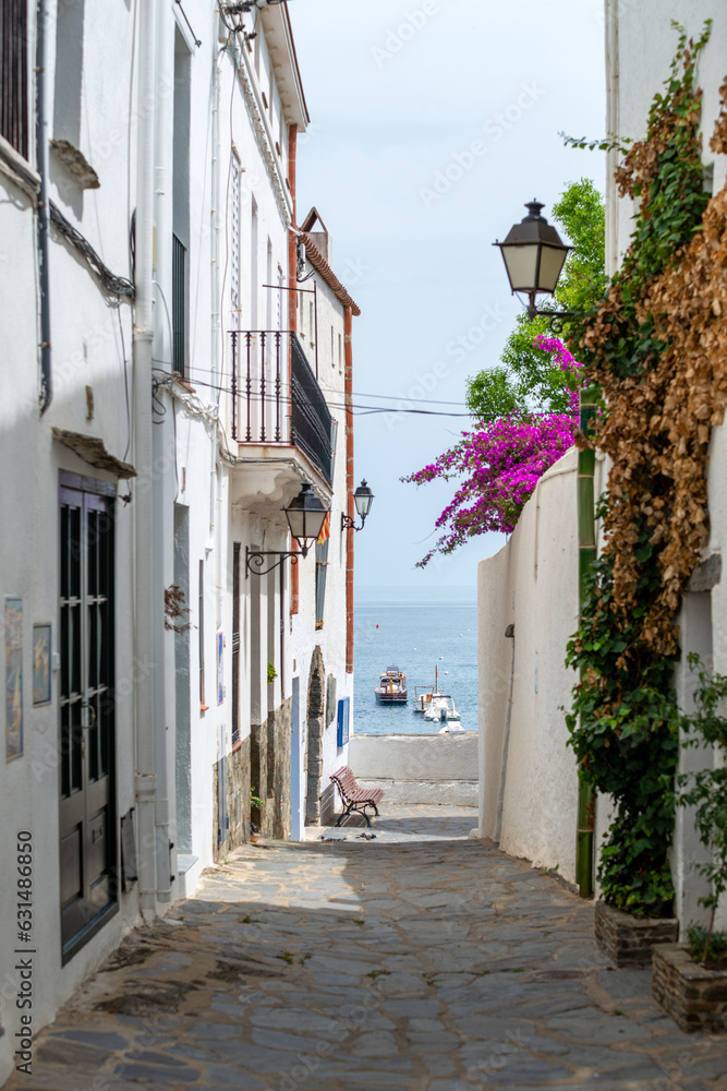Cadaqués, view from a narrow street with traditional white houses to the port with boats - June 10, 2018 - Costa Brava, Catalonia, Spain