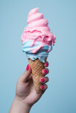 Delicious creamy ice cream in a waffle cone with blue and pink ice cream scoops balls holding in woman's hand isolated on a flat blue background with copy space. Vertical format for stories.