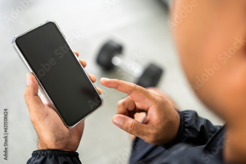 Fototapeta Naklejka Na Ścianę i Meble -  Young Athlete fitness Man Using smartphone in gym. Male Holding Cell Phone Fitness App