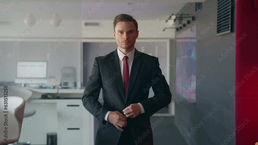 Businessman stands in office, adjusts jacket and looks into camera Businessman stands in office, adjusts jacket and looks into camera