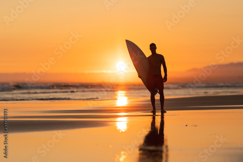 Photography Black silhouette of an attractive man on the shore holding a surfboard at orange