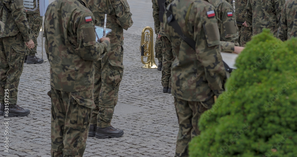 Orkiestra wojskowa na przysiędze wojskowej. Żołnierze muzycy w polskich mundurach z instrumentami. Widoczna złotej barwy trąbka.