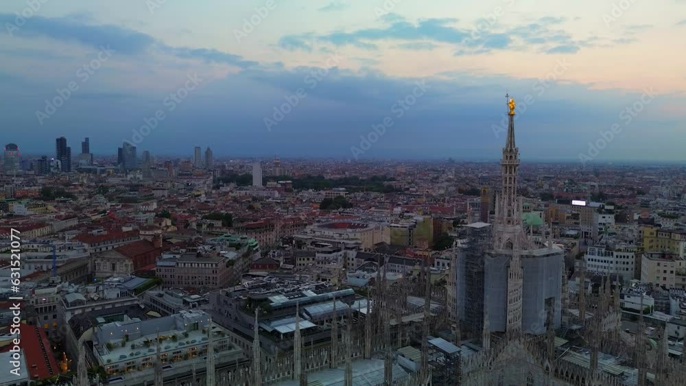 Aerial view of the statue of the Madonna on the central spire of the Duomo and the city's cathedral at dawn. Roofs of houses and skyscrapers. Sun over the horizon. duomo square. Italy Milan 05.08.2023 Aerial view of the statue of the Madonna on the central spire of the Duomo and the city's cathedral at dawn. Roofs of houses and skyscrapers. Sun over the horizon. duomo square. Italy Milan 05.08.2023