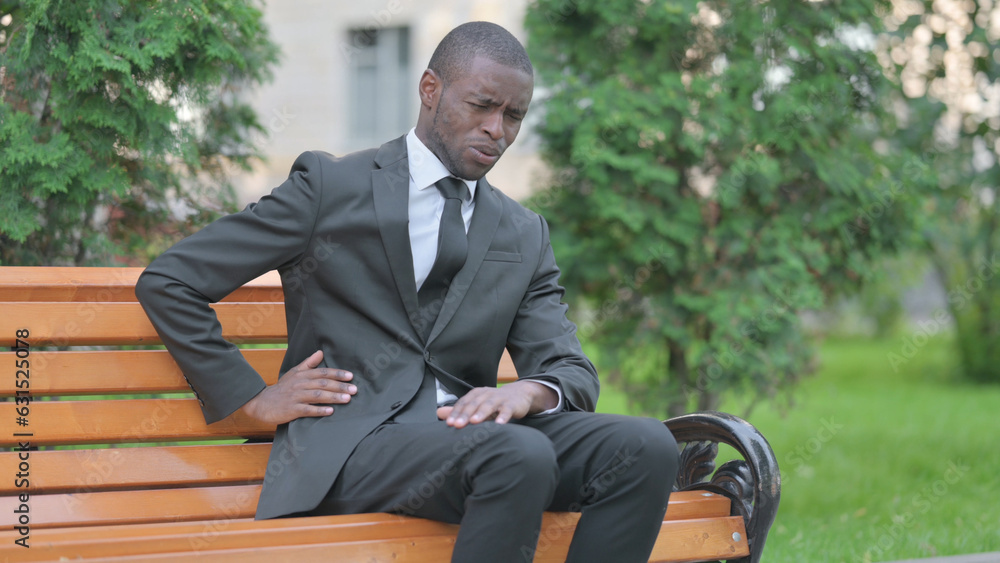 African Businessman Sitting Outdoor with Back Pain African Businessman Sitting Outdoor with Back Pain