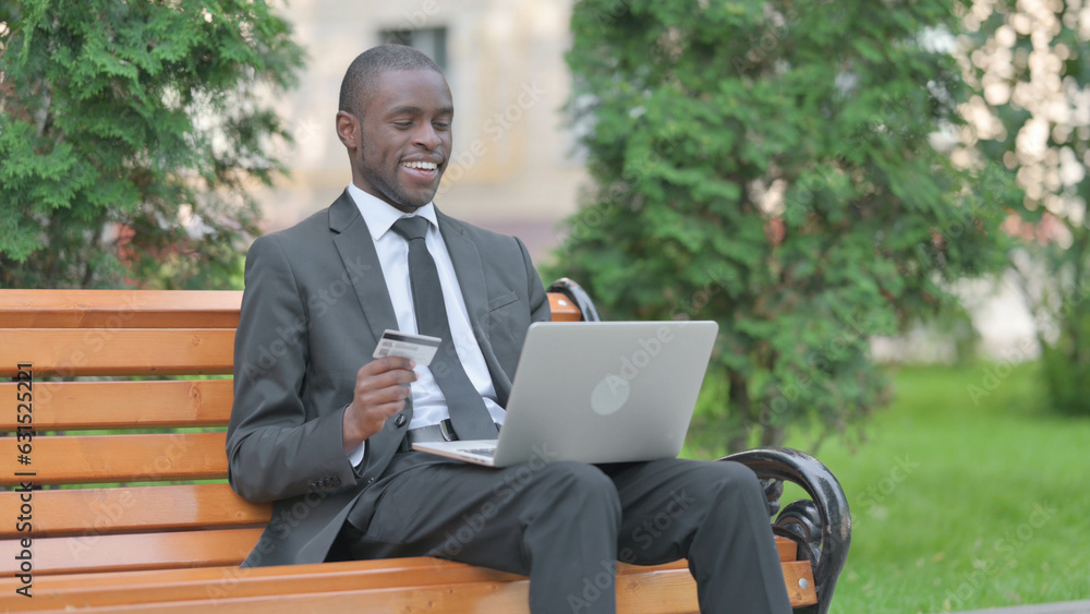 African Businessman Excited for Successful Online Shopping on Laptop Outdoor