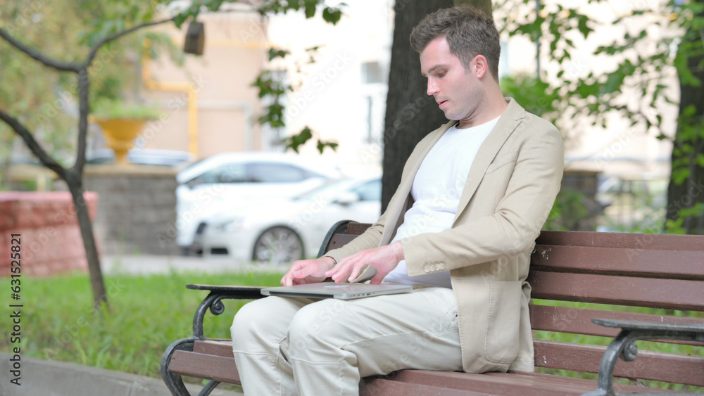Fototapeta premium Casual Young Man Coming, Sitting on Bench and Working on Laptop