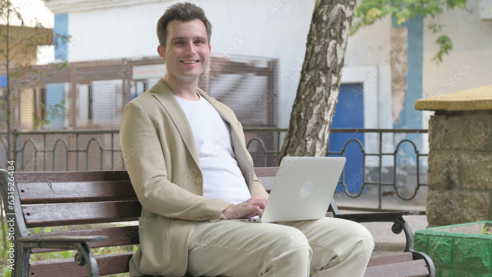 Young Man Smiling at Camera while Working on Laptop Outdoor
