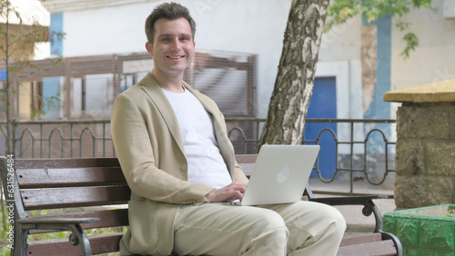 Young Man Smiling at Camera while Working on Laptop Outdoor