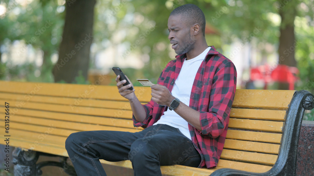 Young African Man Upset by Online Payment Failure on phone while Sitting Outdoor on a Bench Young African Man Upset by Online Payment Failure on phone while Sitting Outdoor on a Bench