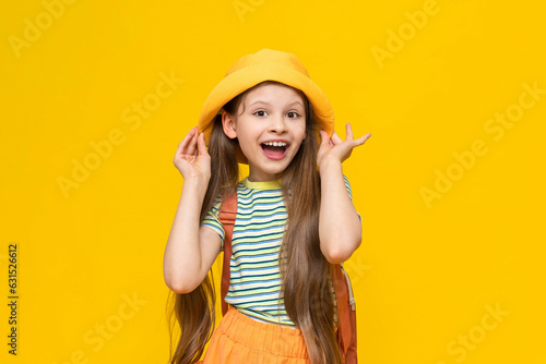 A little girl scout, smiling happily in a summer hat with a backpack. Hiking for children in nature. Yellow isolated bright background.