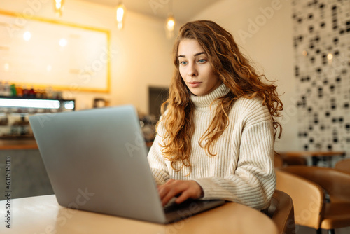 Portrait of a young woman sitting in a cafe at a laptop, working online, freelancing. Сoncept of education, blog. Technologies.