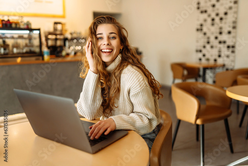Portrait of a young woman sitting in a cafe at a laptop, working online, freelancing. Сoncept of education, blog. Technologies.