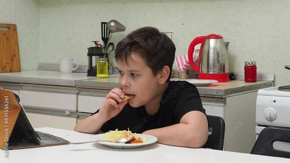 Kid eating eating homemade spaghetti and watching cartoon on tablet, Child boy having breakfast and playing game online on internet with friends before go to school in the morning Kid eating eating homemade spaghetti and watching cartoon on tablet, Child boy having breakfast and playing game online on internet with friends before go to school in the morning