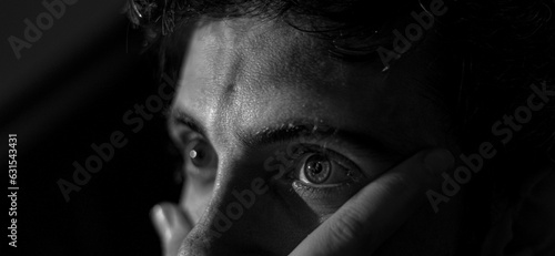 Grayscale closeup of the sad eyes of a young man in a dark environment