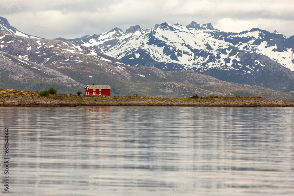a large lake surrounded by snow-covered mountains, with a bright red house in the frame