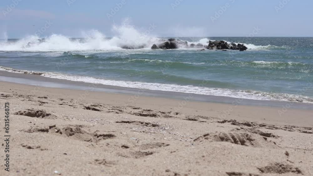 Foamy waves of the sea hitting the sandy beach and the rocks on a sunny day Foamy waves of the sea hitting the sandy beach and the rocks on a sunny day