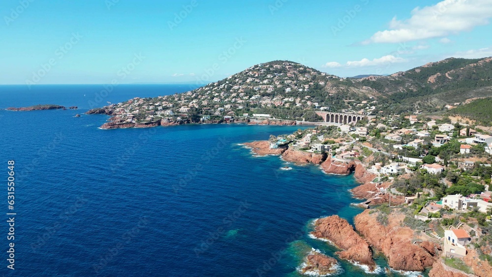 Aerial view of a blue sea and town surrounded by green mountains. Antheor, Massif de l'Esterel.