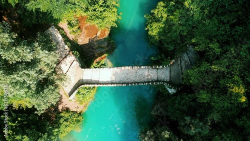 Drone view over a stone bridge above an azure river between green trees photo