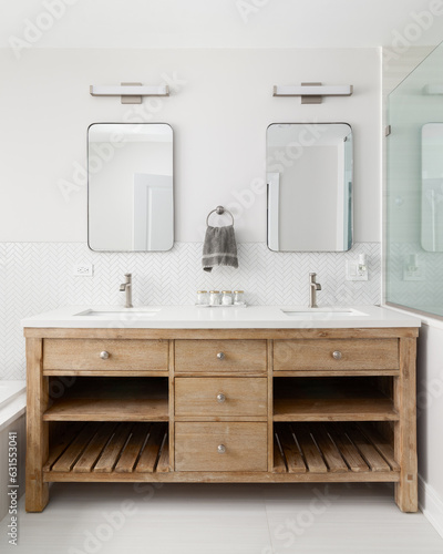 A cozy bathroom detail with a white oak vanity cabinet  white countertop  bronze faucets and lights and a white herringbone tile backsplash.  