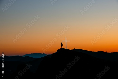 Silhouette of a person standing near a cross on a hill during the sunset