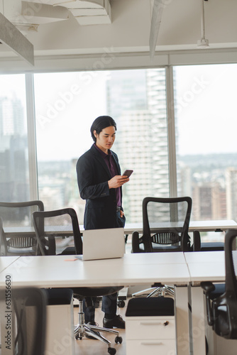 Serious Asian businessman wearing stylish black suit holding mobile phone standing in meeting room