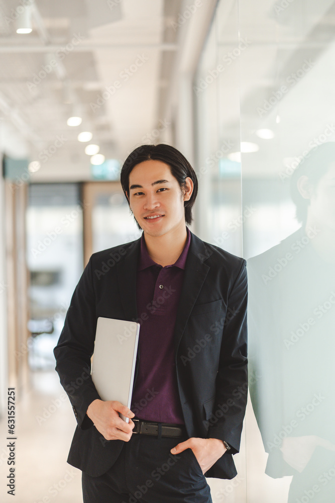 Fototapeta premium Portrait of Asian man manager wearing black suit formal wear holding laptop, looking at camera
