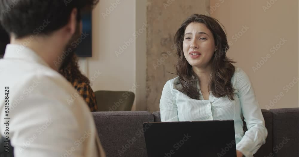 Beautiful young female talking with her male colleagues while working on her laptop and resting on the sofa, trucking movement Beautiful young female talking with her male colleagues while working on her laptop and resting on the sofa, trucking movement