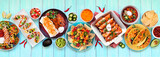 Mexican food table scene. Top down view on a blue wood banner background. Tacos, burrito plate, nachos, enchiladas, tortilla soup and salad. Copy space.
