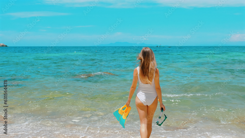 Woman in swimwear walks in sea water with snorkel mask and fins. Prepare for underwater snorkeling experience. Concept of tropical beach vacation. Woman in swimwear walks in sea water with snorkel mask and fins. Prepare for underwater snorkeling experience. Concept of tropical beach vacation.