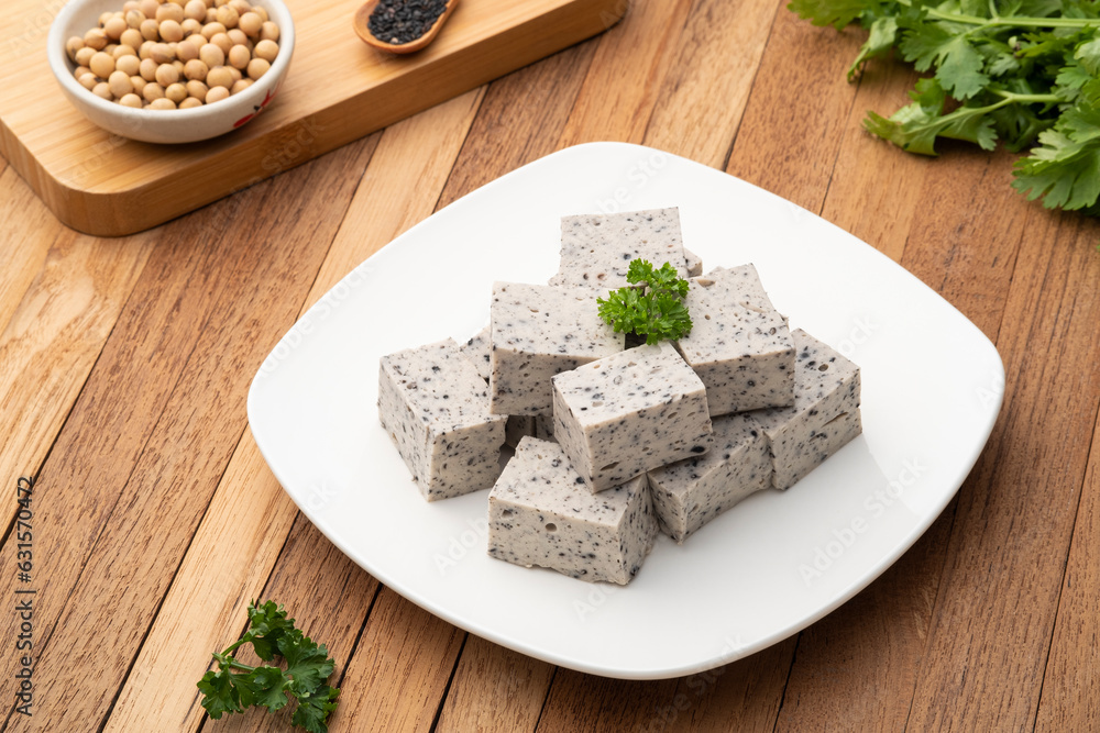 Sliced piece of Tofu mix black sesame seeds in white plate on wooden table Sliced piece of Tofu mix black sesame seeds in white plate on wooden table