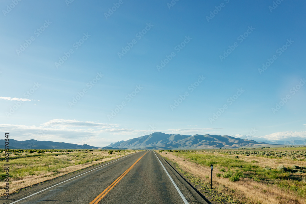 Beautiful road landscape with road signs, mountains, highway and blue sky with fluffy clouds on a sunny summer day. American landscape with a wide highway