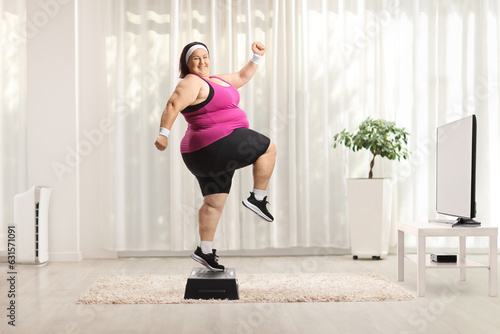 Cheerful overweight woman exercising step aerobics at home