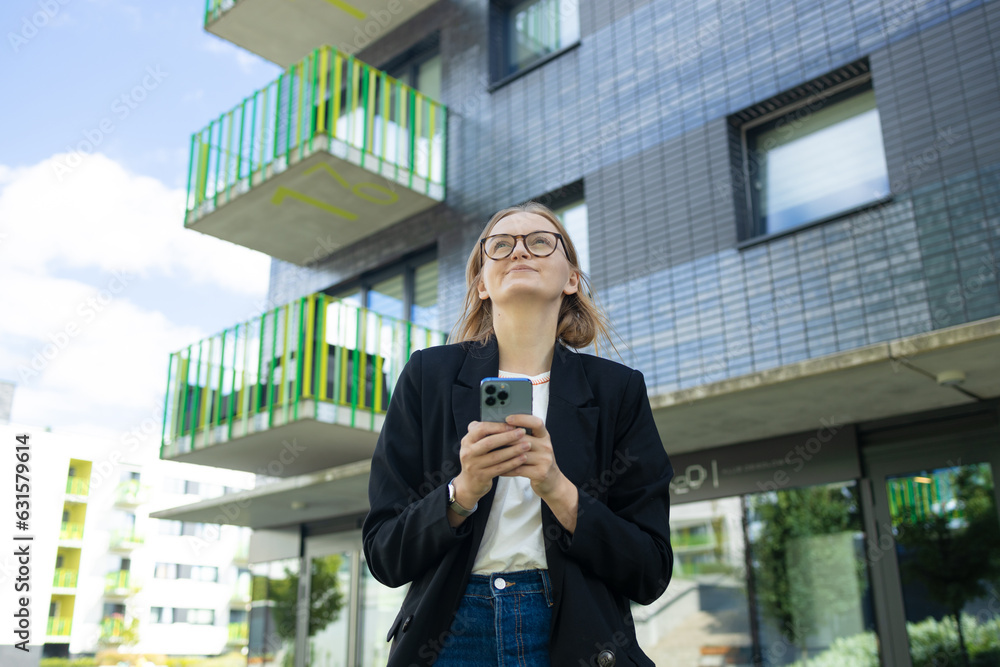 Smiling businesswoman using her phone outdoors. Small business entrepreneur looking at her mobile phone and smiling while communicating with her office colleagues. High quality photo Smiling businesswoman using her phone outdoors. Small business entrepreneur looking at her mobile phone and smiling while communicating with her office colleagues. High quality photo