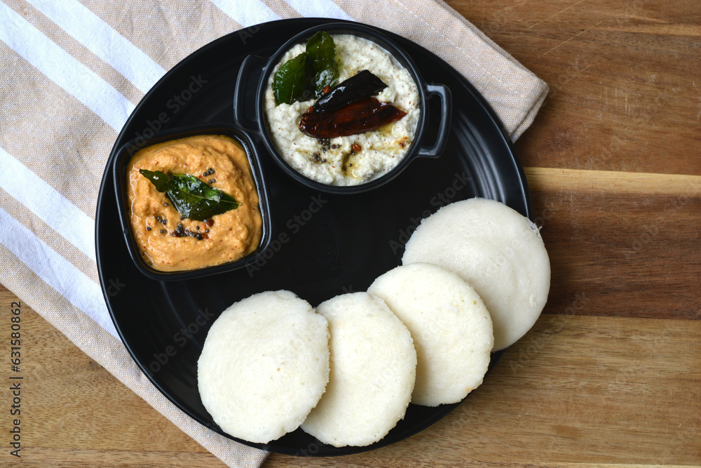 Idli and chutney in a black plate on wooden board. South Indian idlis. Idli and chutney in a black plate on wooden board. South Indian idlis.